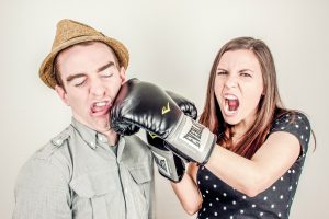 Una mujer con guantes de boxeo golpea a un hombre para simbolizar una de las 4 toxinas del trabajo en equipo: el menosprecio